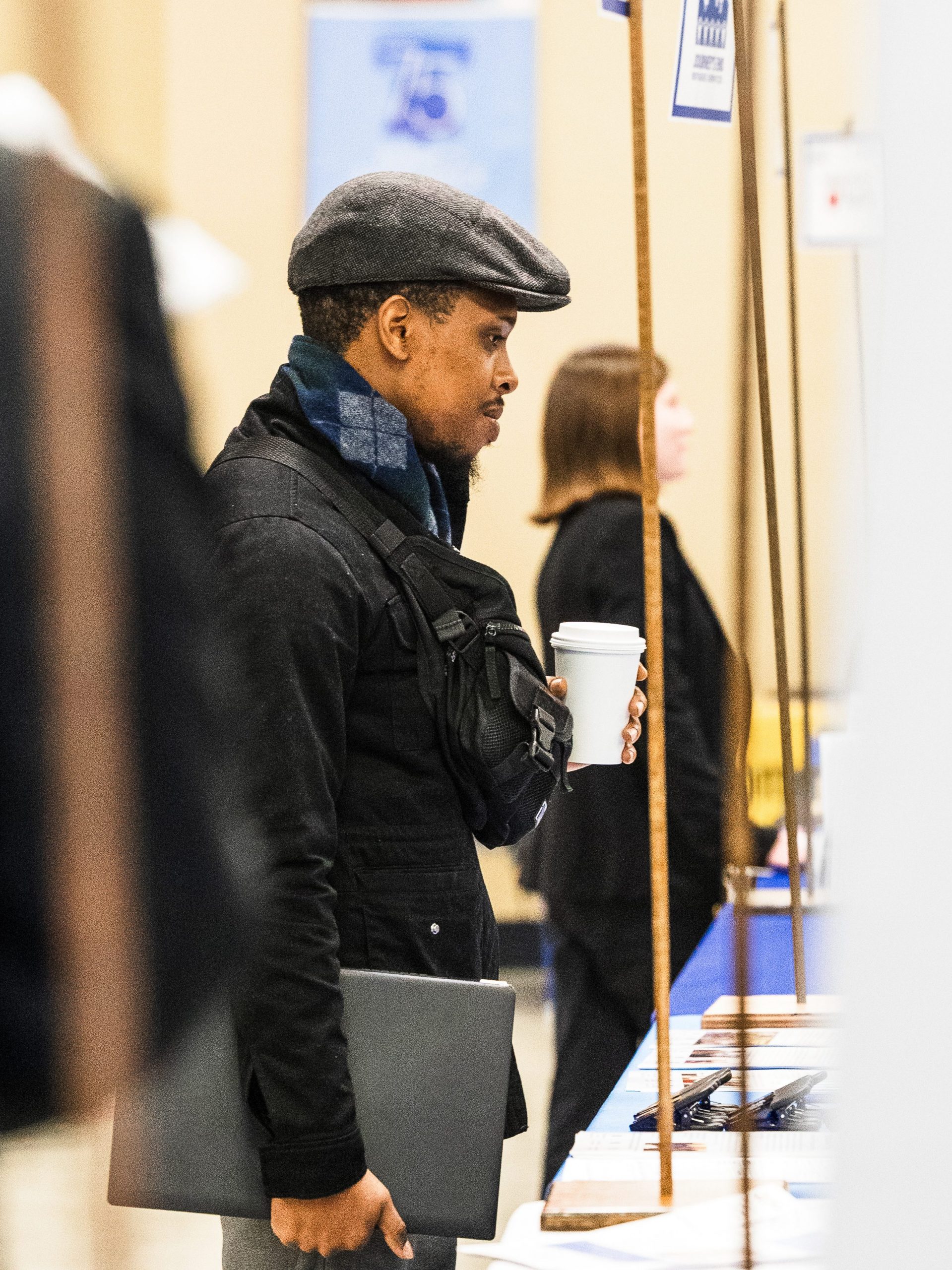 Student holding a coffee and laptop looking at artwork