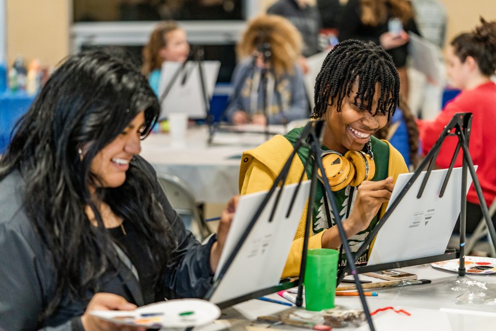 students smiling painting on easels 