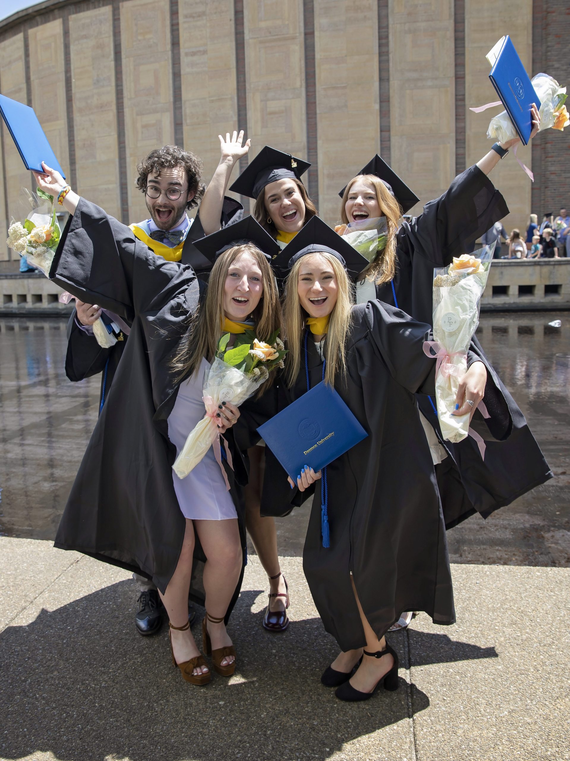 Students in commencement robes posing outside of kleinhans music hall.