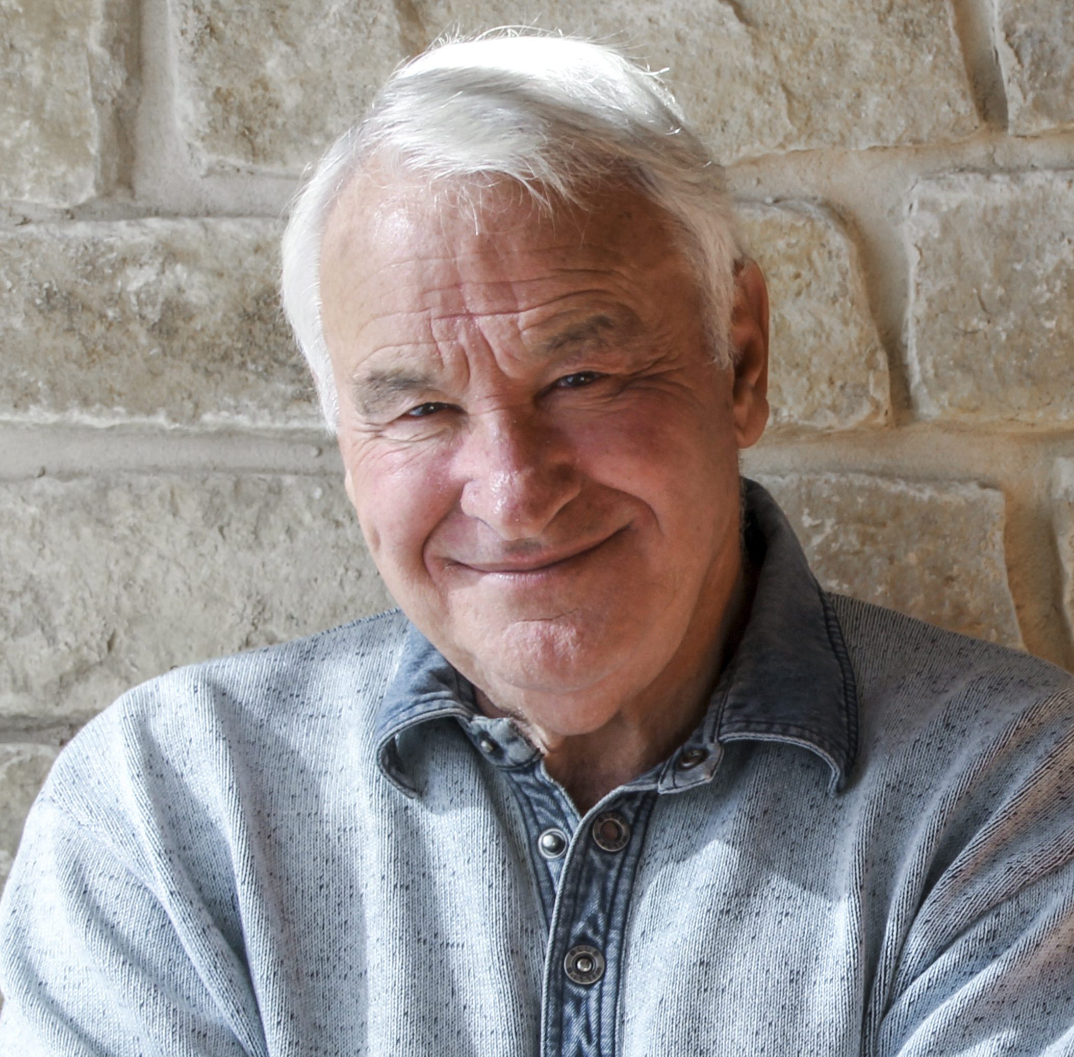 B. Thomas Golisanon standing against a brick wall with his arms crossed smilling