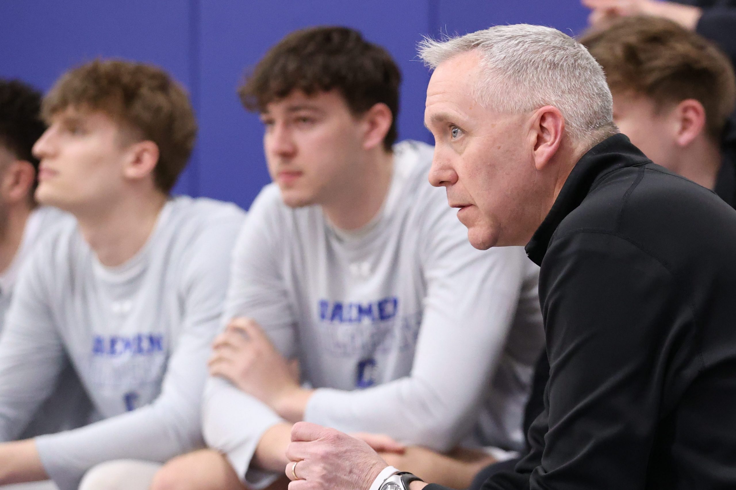 Coach MacDonald sitting on bench with players watching the game.