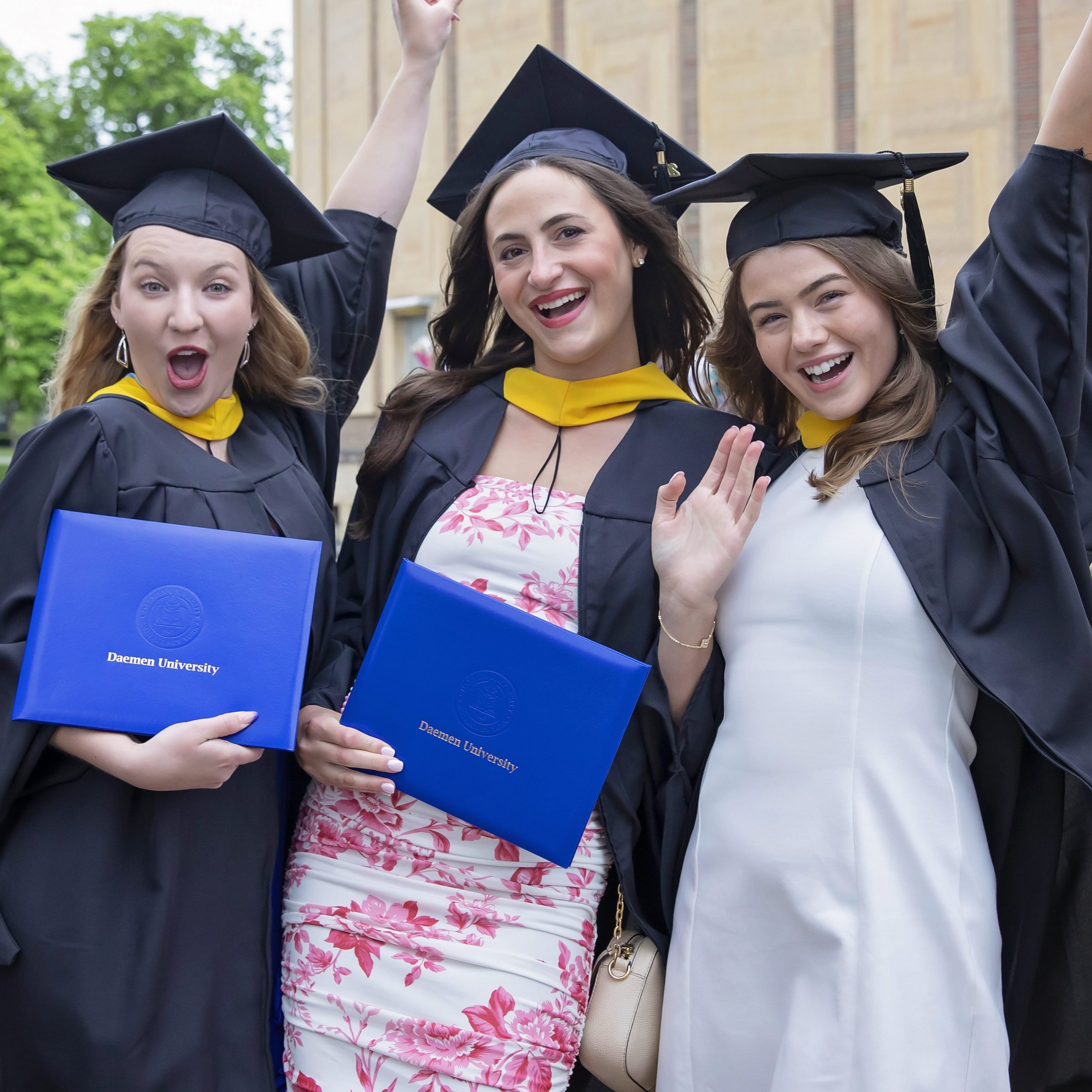 Three female graduates outside of kleinhans music hall