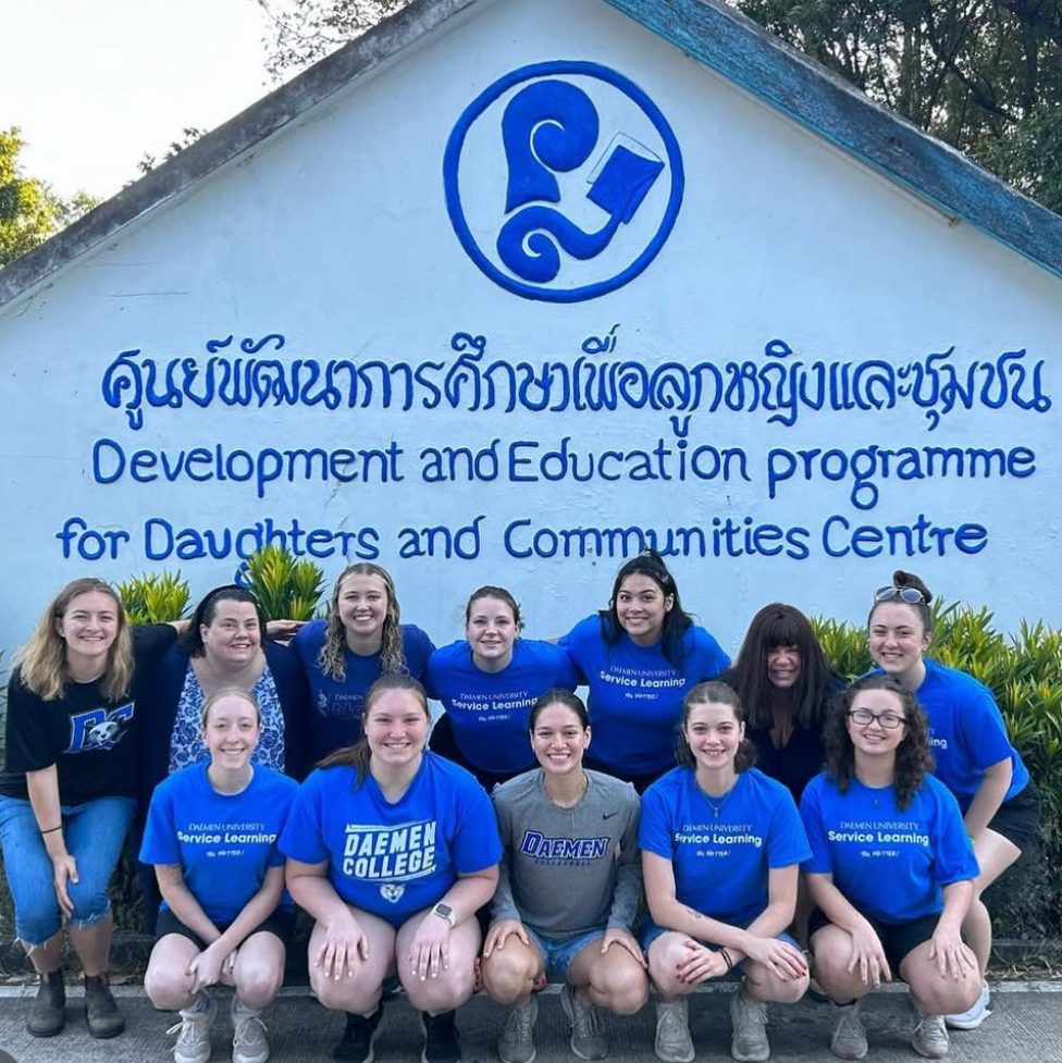Service trips students croched in front sign