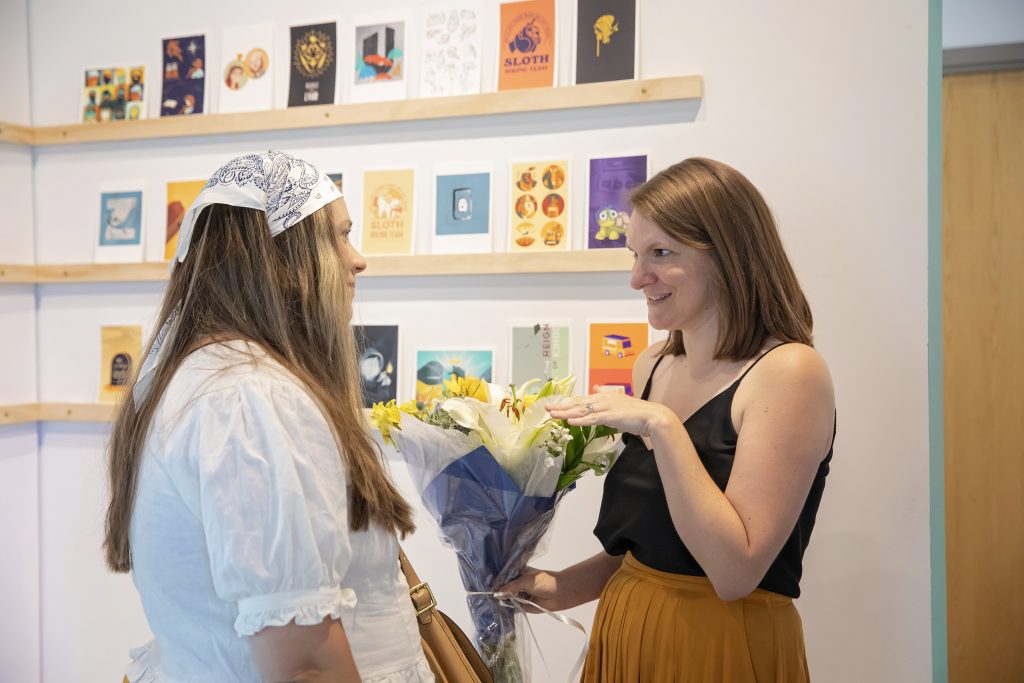Daemen alum Katie Arcara holds flowers while speaking with a guest at her art exhibit