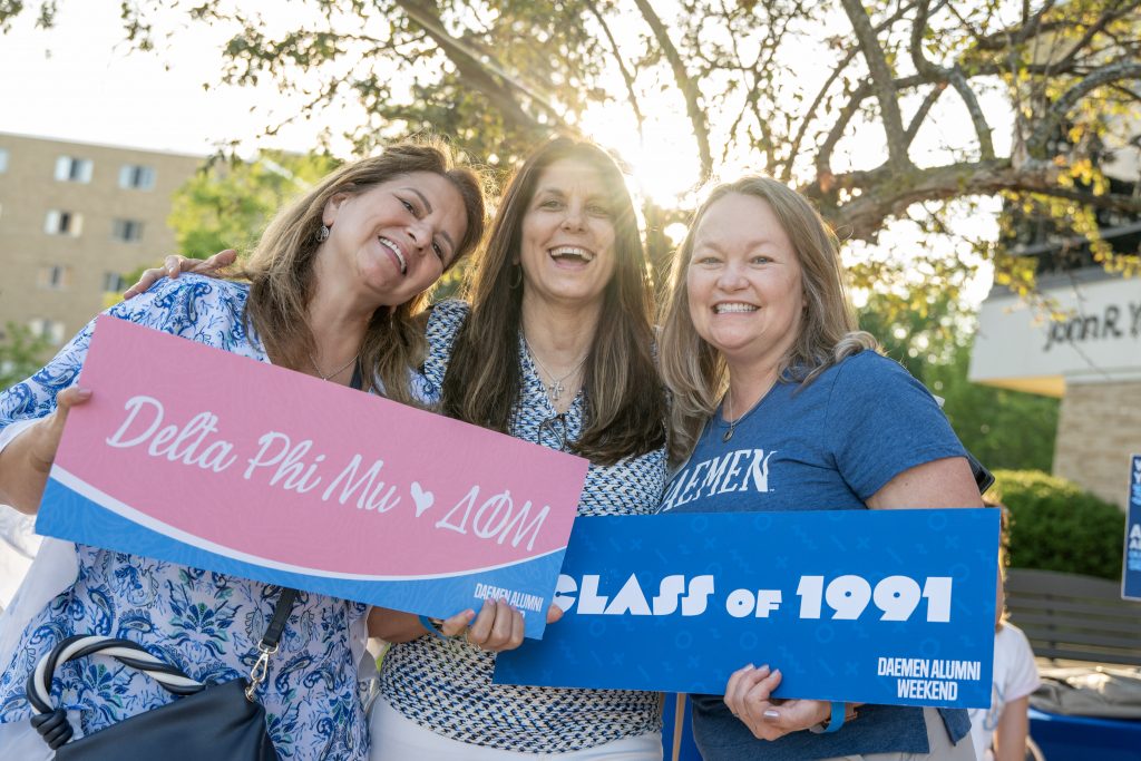 Three members of Delta Phi Mu standing together holding signs