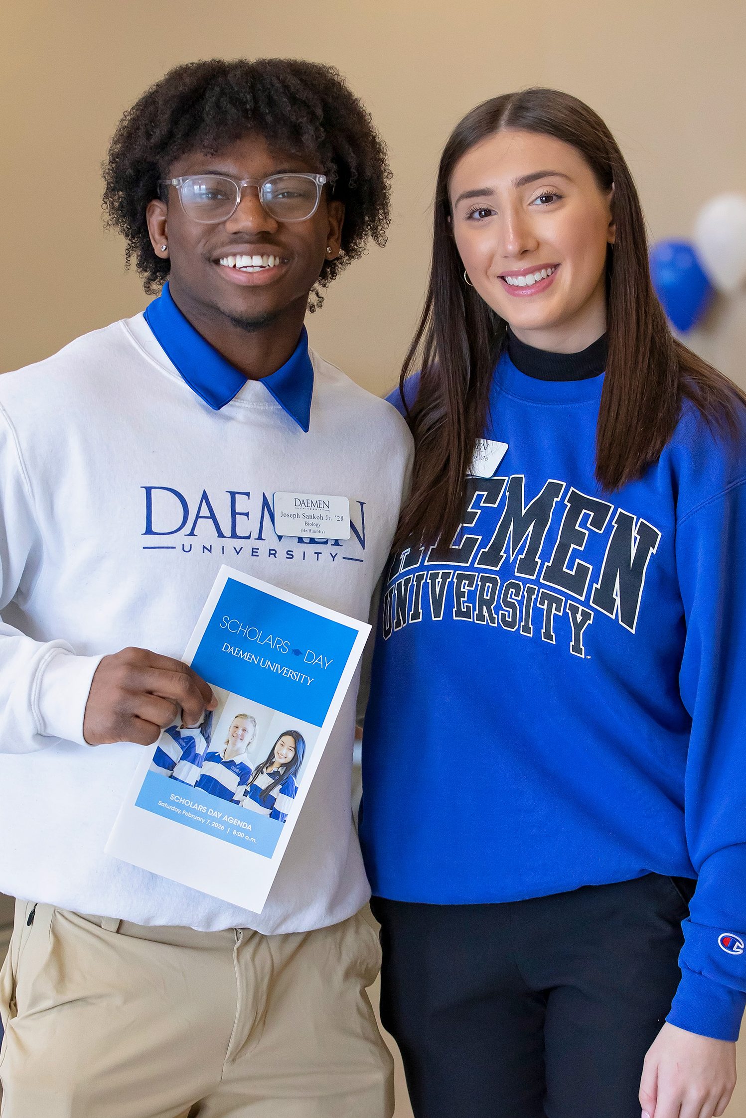 A male and female student wearing Daemen crew sweatshirts standing together